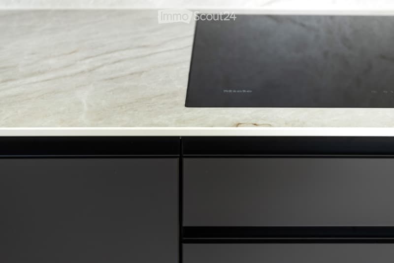 Modern kitchen with a sleek black induction cooktop on a light marble countertop, surrounded by dark cabinets.
