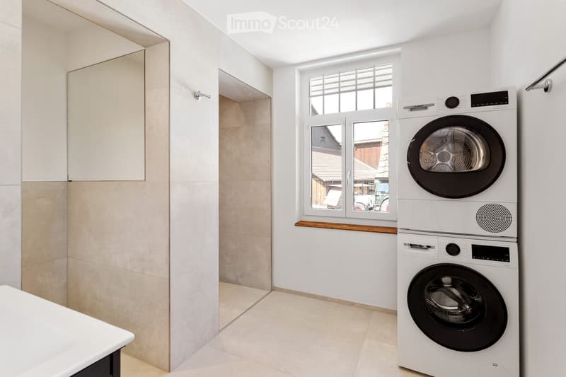 Modern bathroom with a stacked washing machine and dryer, a window with wooden sill, and a built-in cabinet.