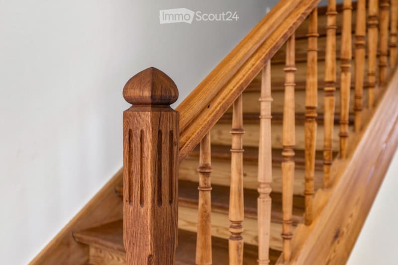 Wooden staircase with ornate balusters and a polished handrail, featuring a decorative newel post at the bottom.