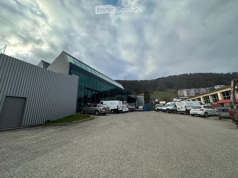 Modern industrial building with a glass facade and a parking lot with several vehicles, including vans and cars.