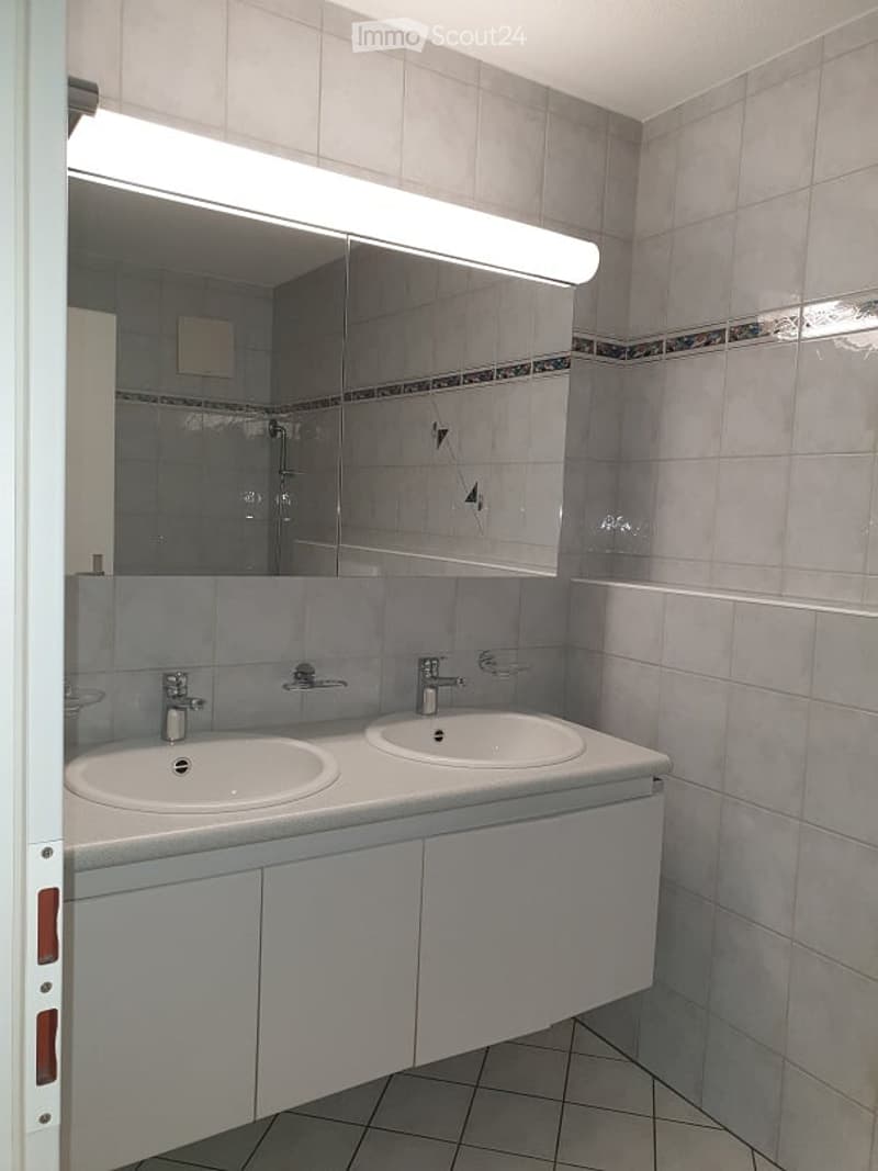 Modern bathroom with two sinks, a large mirror, and white tiled walls and floor.
