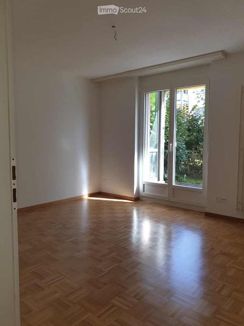 Empty room with wooden flooring, large sliding glass doors, and natural light coming in.