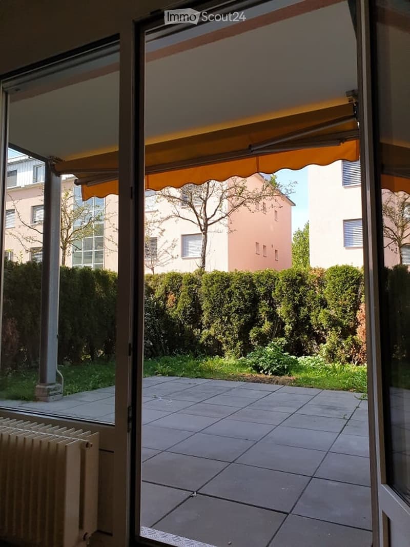 Balcony with tiled floor, yellow awning, view of garden and neighboring buildings.