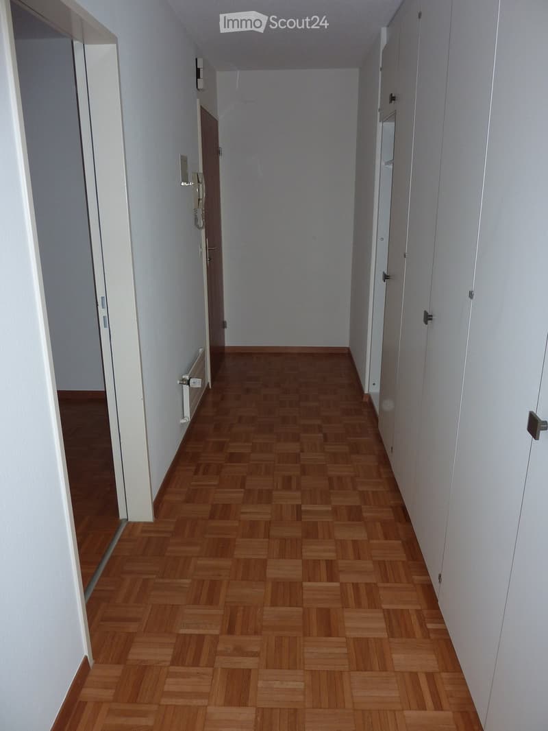 Empty hallway with wooden herringbone flooring, white walls, and several doors leading to other rooms.