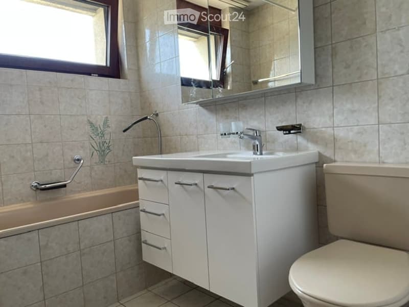Modern bathroom with white cabinetry, a sink, a toilet, a bathtub, and a mirror above the sink. The walls are tiled with a decorative plant design.