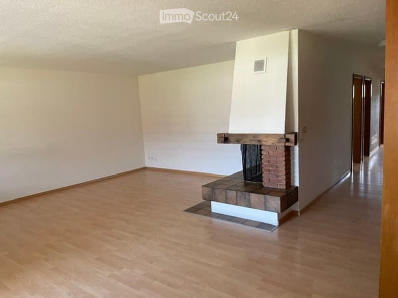 Empty room with wooden flooring, white walls, and a fireplace with a brick surround.