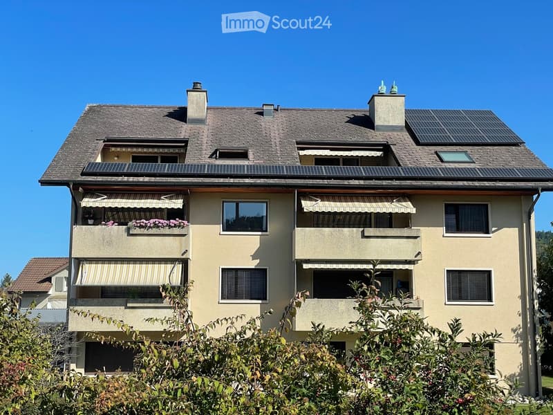 Two-story house with solar panels on the roof, multiple balconies with flower boxes, and striped awnings.