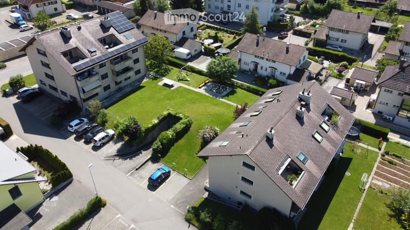 Aerial view of a residential area with multiple houses, green lawns, parking spaces, and solar panels on rooftops.