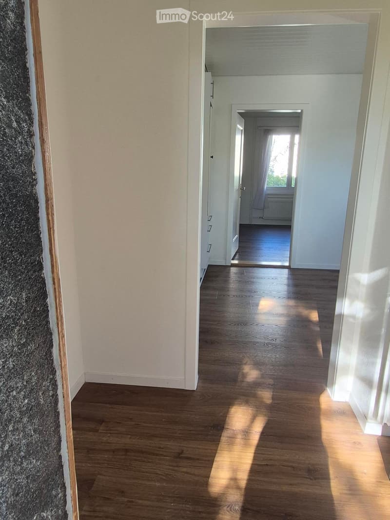 Empty hallway with wooden flooring, white walls, and open doors leading to other rooms.