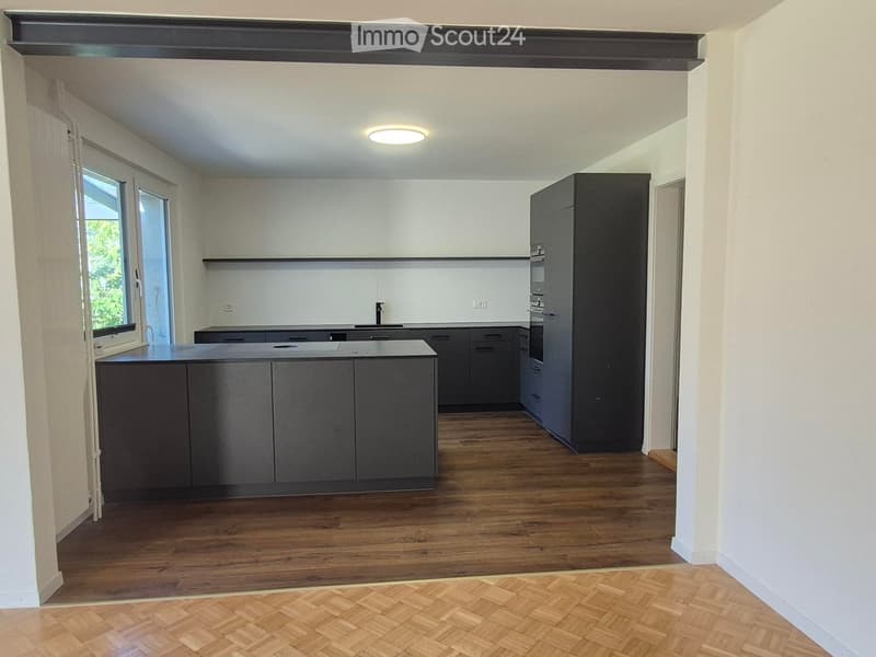 Modern kitchen with dark grey cabinets, a central island, and a wooden floor. Features include a built-in oven and ample storage space.