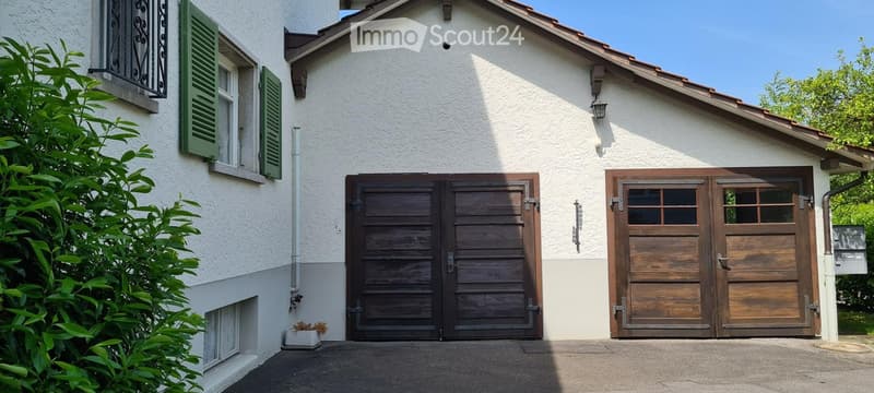 Two-story house with white exterior, green shutters, and two large wooden garage doors.