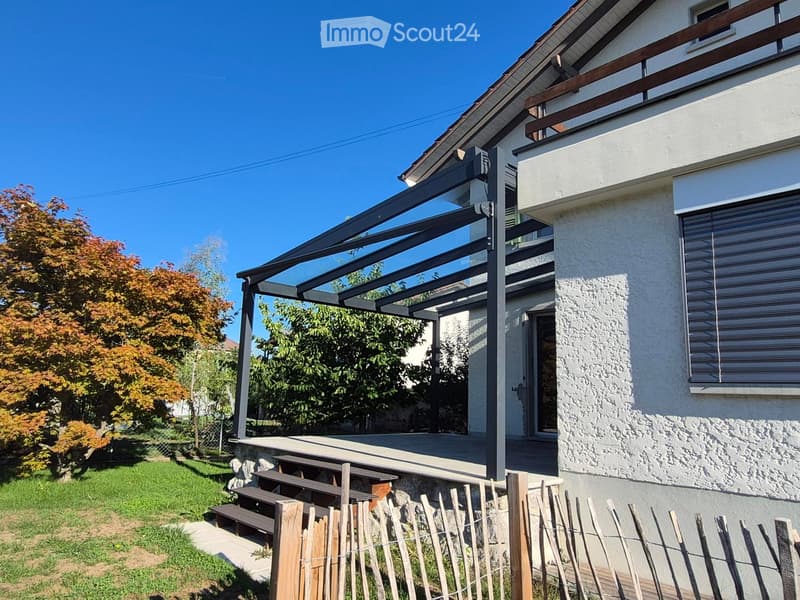 Two-story house with a covered patio, wooden fence, and autumn-colored trees in the yard.