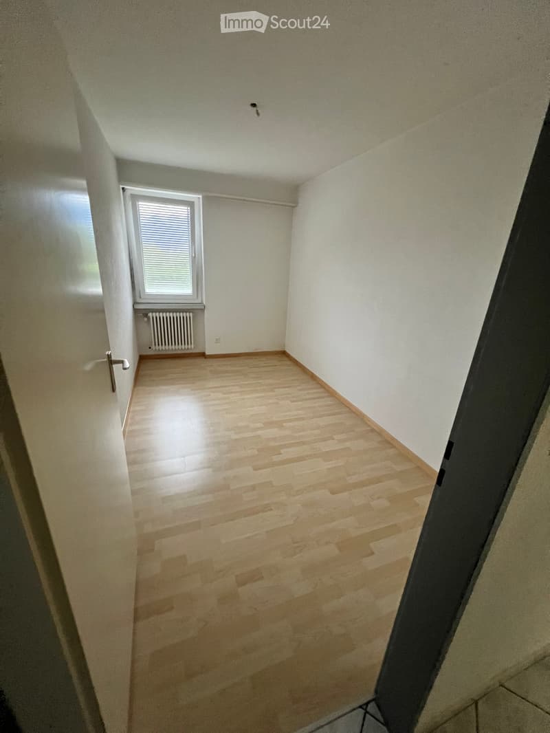 Empty room with wooden flooring, white walls, and a window with blinds. A radiator is visible below the window.