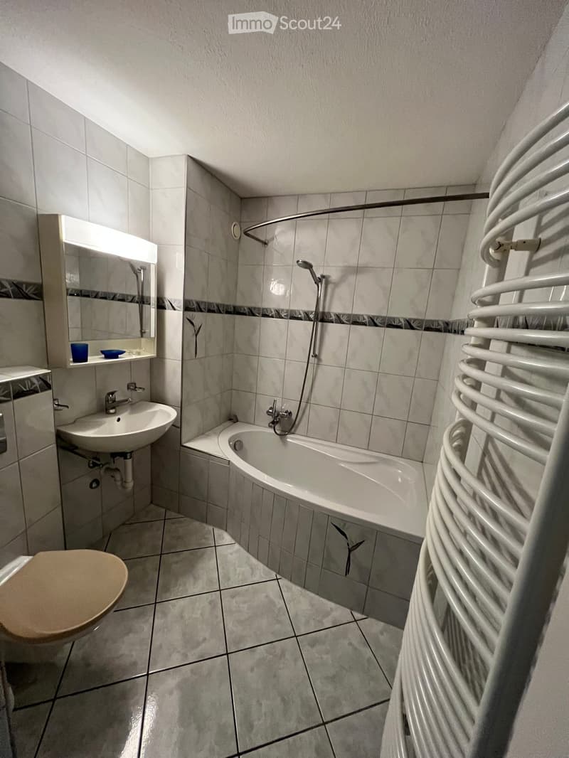 Modern bathroom with tiled walls and floor, featuring a sink, toilet, bathtub, mirror, and radiator.