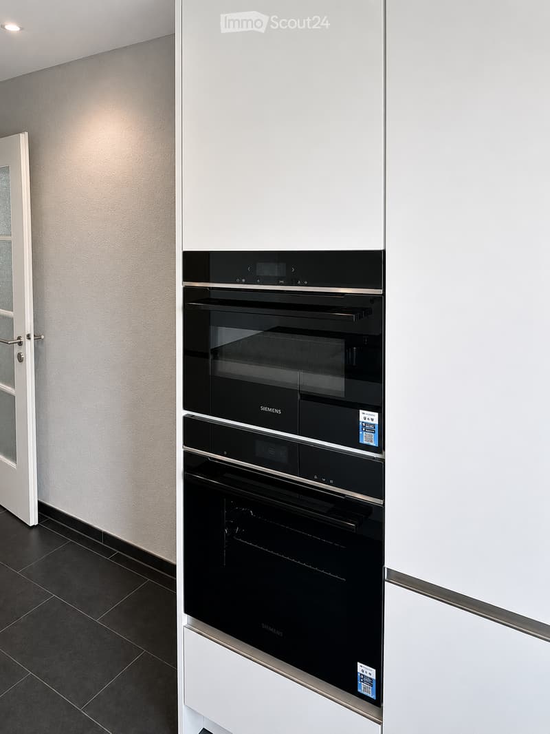 Modern kitchen with sleek black Siemens oven, white cabinetry, and dark tiled floor.