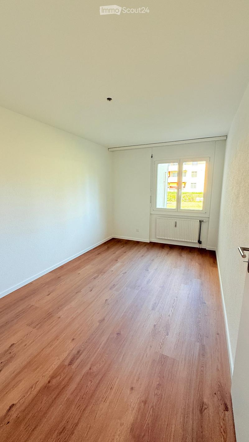 Empty room with wooden flooring, white walls, and a window with blinds. A radiator is visible below the window.