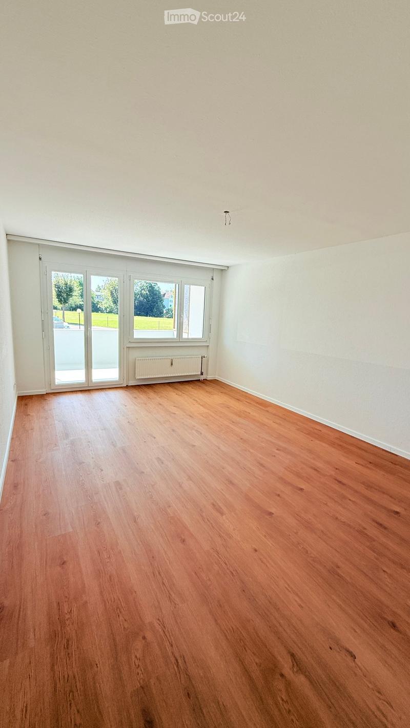 Empty room with wooden flooring, white walls, large windows, and a radiator. No furniture or equipment present.