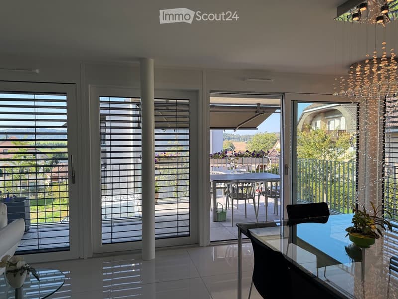 Modern living room with large sliding glass doors leading to a balcony, white sofa, coffee table, dining table, and chairs.