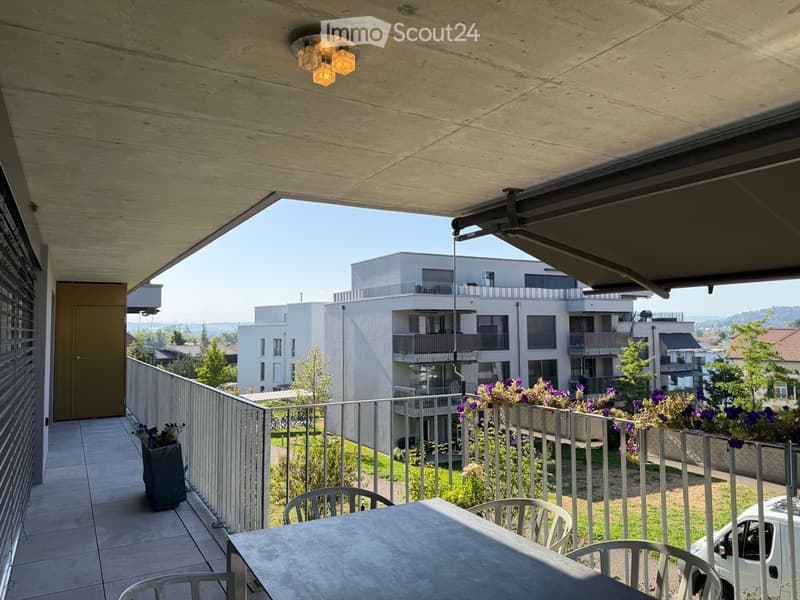 Balcony with a modern design, featuring a table and chairs, a potted plant, and a view of a contemporary residential building complex.