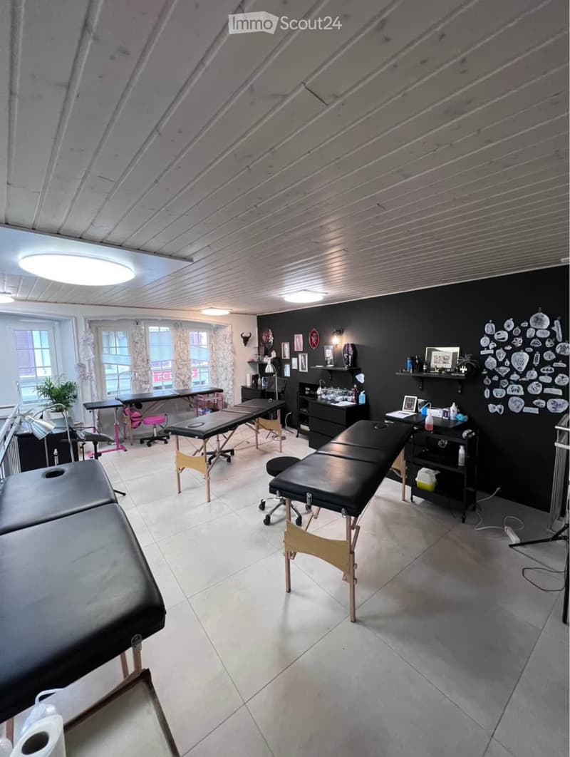 A well-lit room with multiple massage tables, chairs, shelves, and decorative items on the walls.