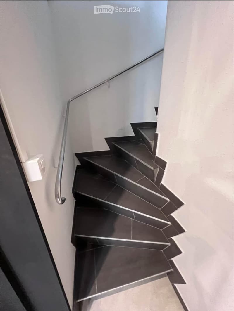 Modern staircase with dark tiled steps and a sleek metal railing, set against light-colored walls.