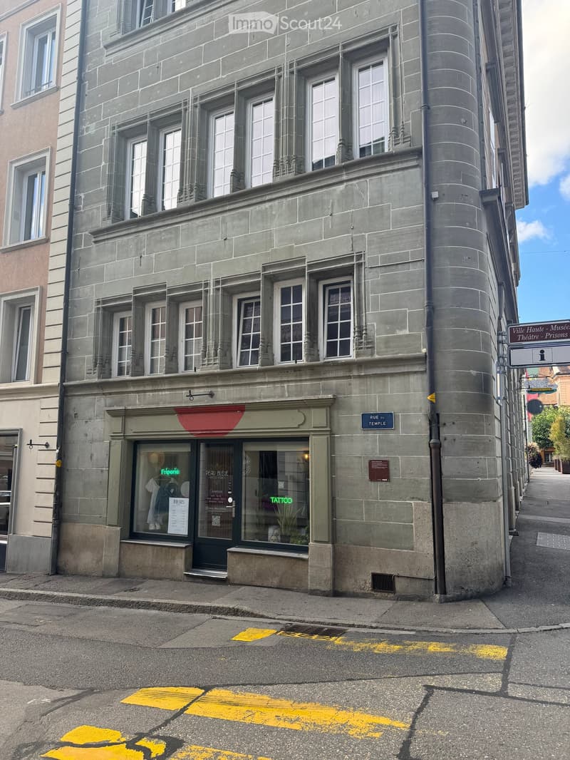 Four-story stone building with multiple windows, a storefront with glass display, and a sign reading "Rue du Temple".
