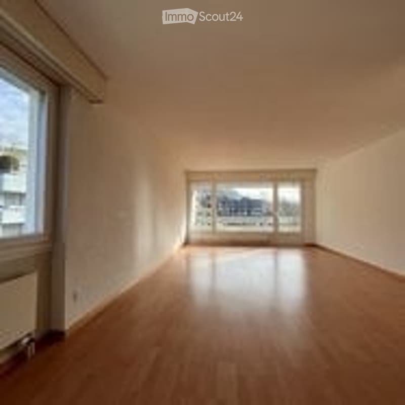 Completely empty room with wooden flooring, white walls, and large windows with a view of the city.