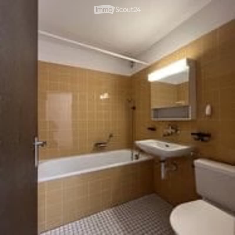 Bathroom with a bathtub, sink, mirror, and toilet. The walls are tiled in a warm, earthy tone, and the floor has a checkered pattern.