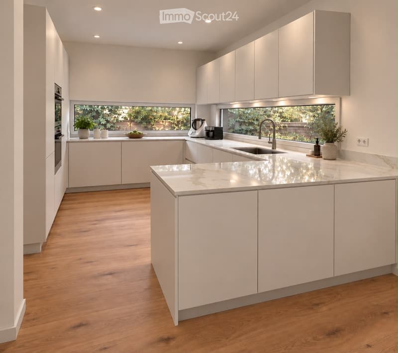Modern kitchen with white cabinets, marble countertops, wooden flooring, and large windows overlooking a garden. Features include a central island, sink, coffee maker, blender, and decorative plants.