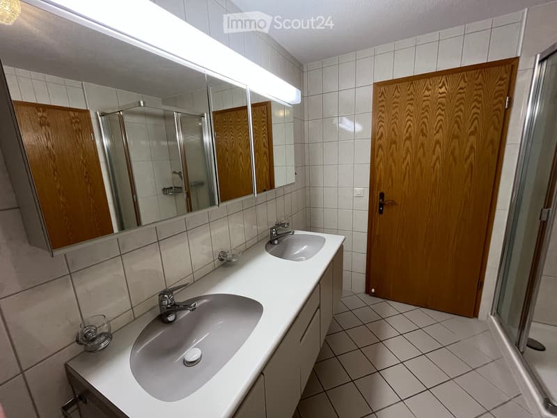 Modern bathroom with two sinks, a large mirror, wooden cabinets, and tiled walls and floor.