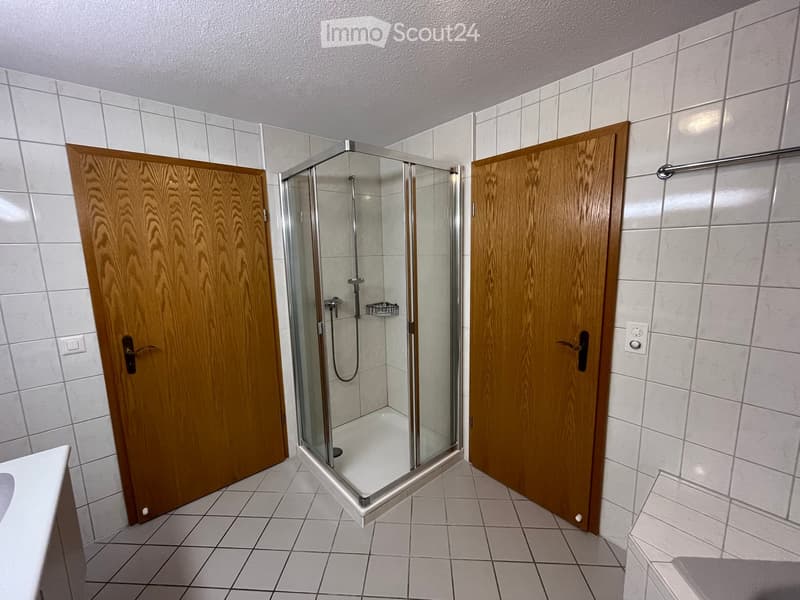 Bathroom with tiled walls and floor, featuring a glass-enclosed shower stall and two wooden doors.