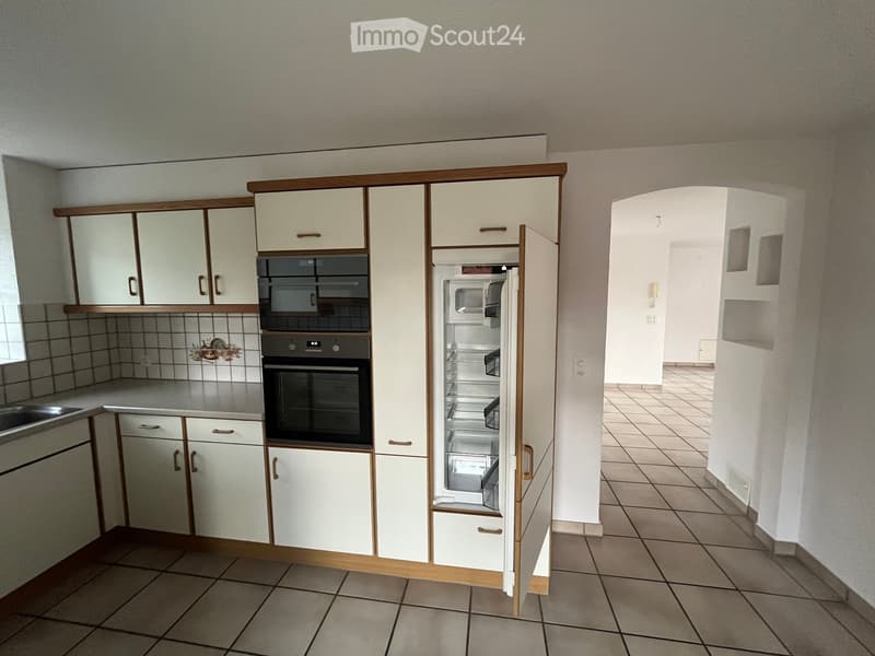 A modern kitchen with white cabinets, a stainless steel oven, a refrigerator, and a sink, featuring tiled walls and floors.