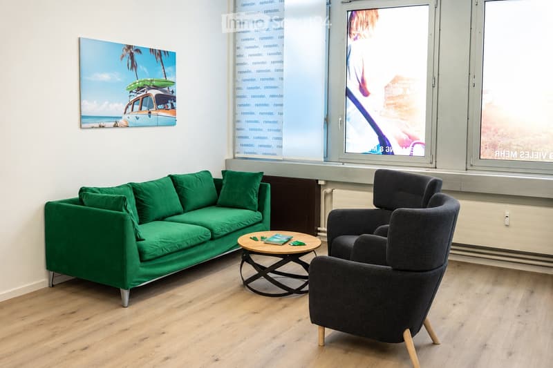 Modern living room with green sofa, dark grey armchair, round coffee table, and a large picture frame on the wall.