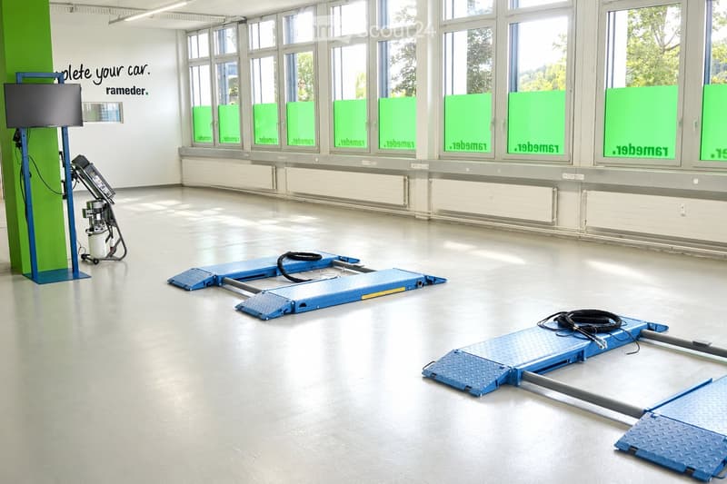 Empty room with large windows, white walls, and a smooth concrete floor. Contains blue ramps and a small machine on the left side.