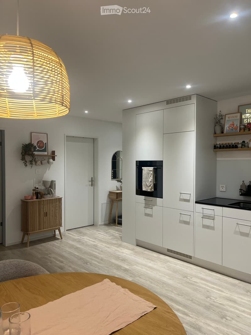 Modern kitchen with white cabinets, a round wooden dining table, a coffee maker, and a large hanging light fixture.