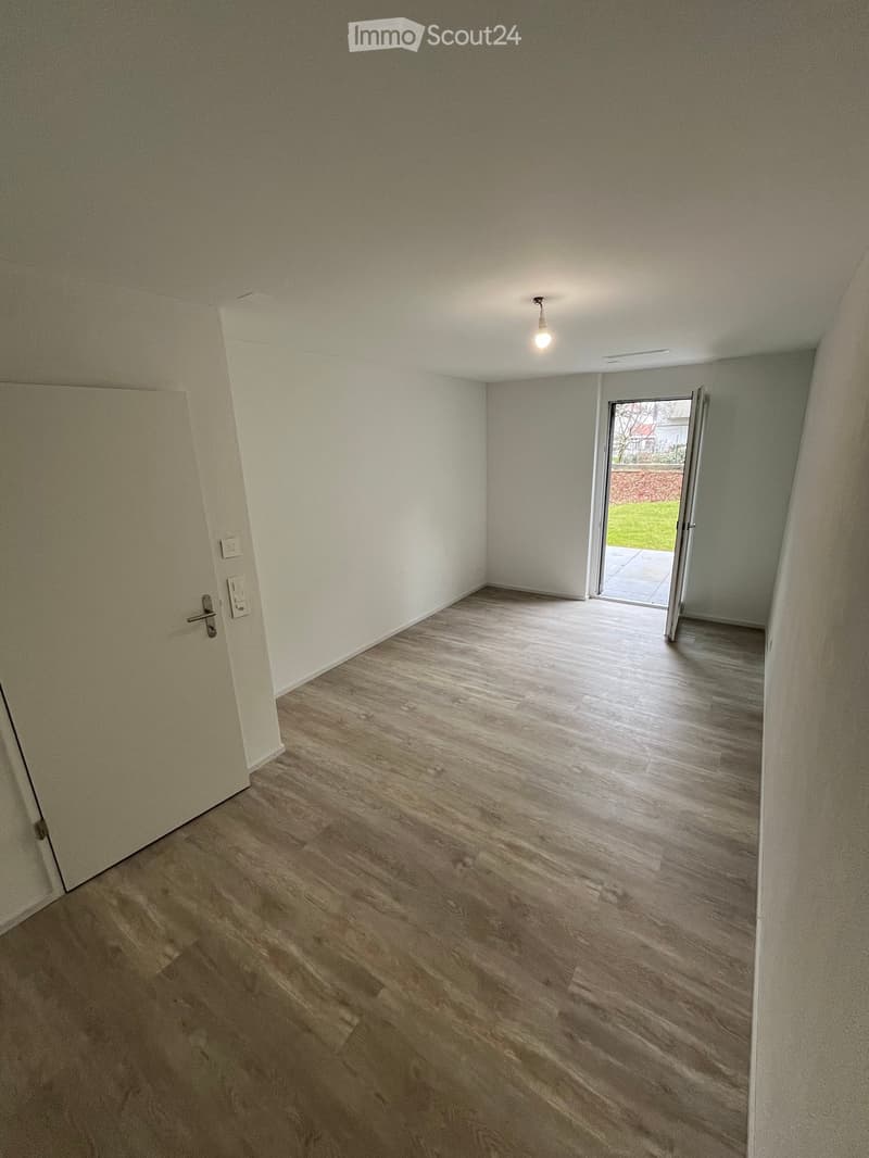 Empty room with wooden flooring, white walls, and a sliding door leading to an outdoor area.