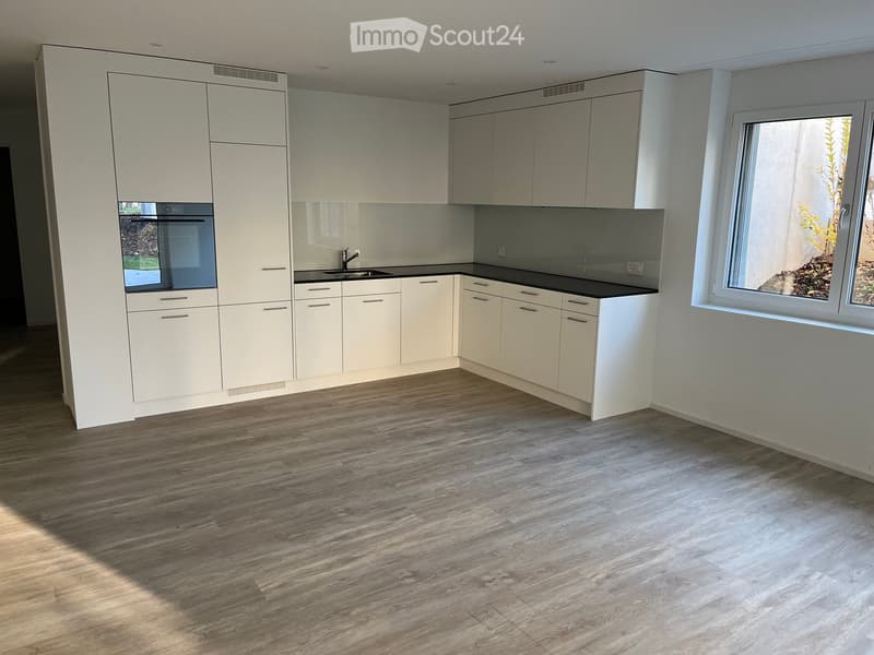 Modern kitchen with white cabinets, black countertops, and a wooden floor. Features an oven, sink, and faucet.