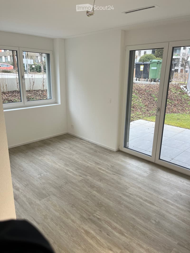 Empty room with light-colored walls, wooden flooring, and large sliding glass doors leading to a patio area.