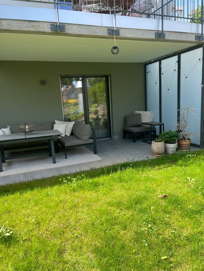 Outdoor patio area with a sofa, table, chairs, and potted plants, connected to a grassy lawn.