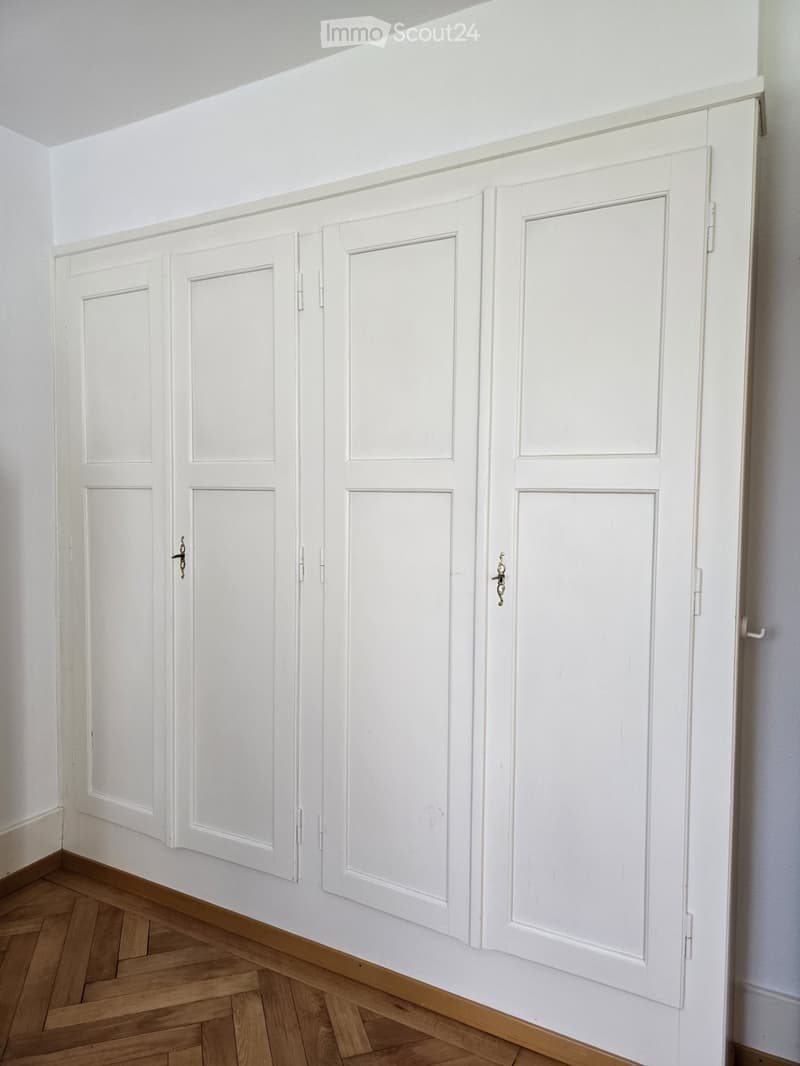 Empty hallway with white paneled doors and wooden herringbone flooring.