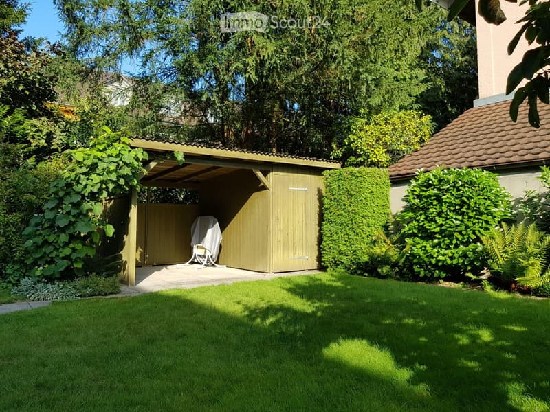 Well-maintained garden with a covered patio area, a wooden shed, and a covered seating area with a chair and tablecloth.