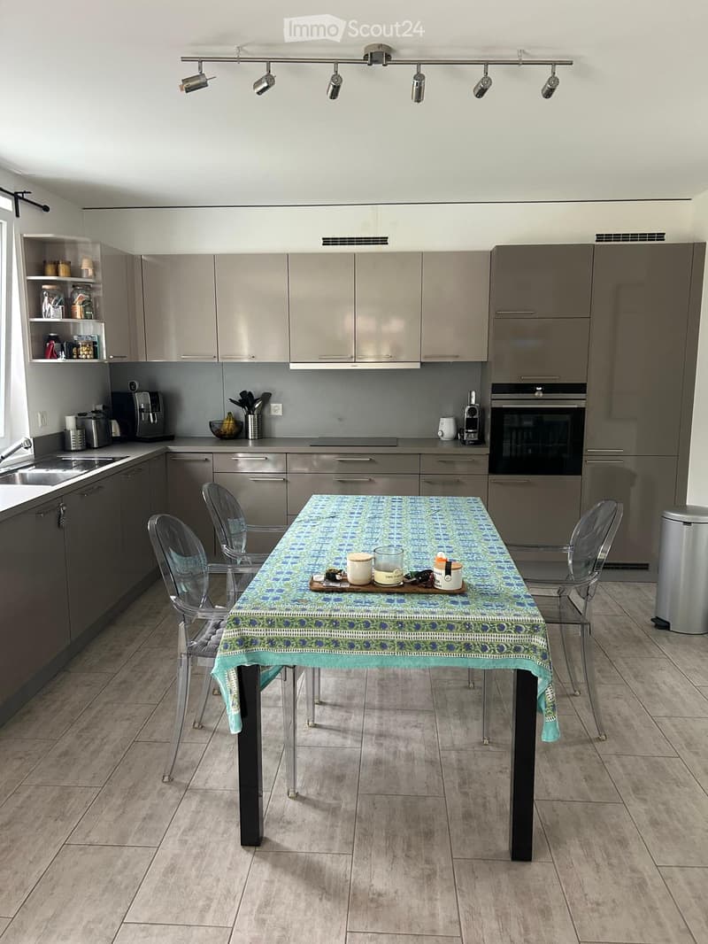Modern kitchen with grey cabinets, stainless steel appliances, a dining table with chairs, and various kitchen items on the counter.