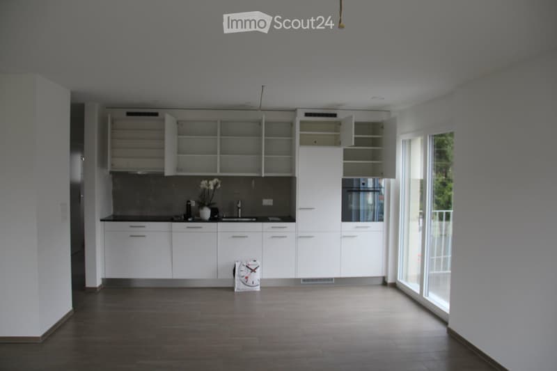 Modern kitchen with white cabinets, dark countertops, and a large window. Includes a sink, faucet, flower vase, and a clock on the floor.