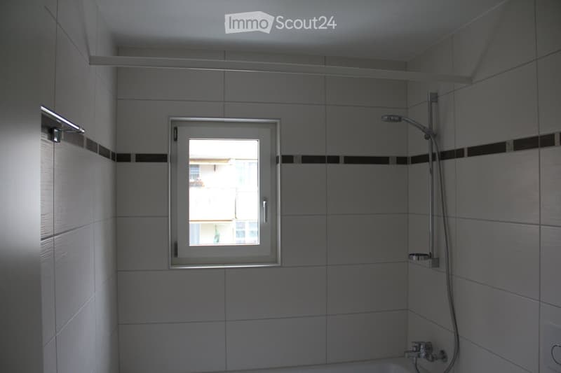 Modern bathroom with tiled walls, a showerhead, a window offering a view, and a faucet.