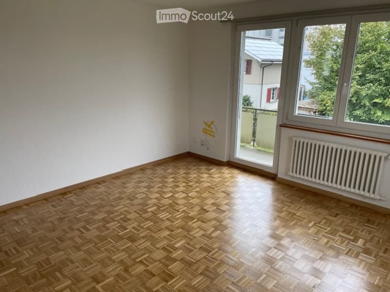 empty room, white walls, wooden parquet floor, sliding glass doors leading to a balcony, radiator