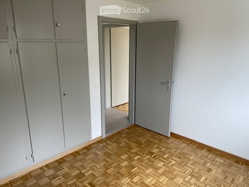 Empty room, wooden floor, gray door, white walls, closets, doorway to another room