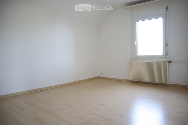 Empty room with light wooden flooring, white walls, a window with white frame, and a radiator below the window.
