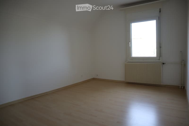 Empty room with wooden flooring, white walls, and a single window with a radiator below it.