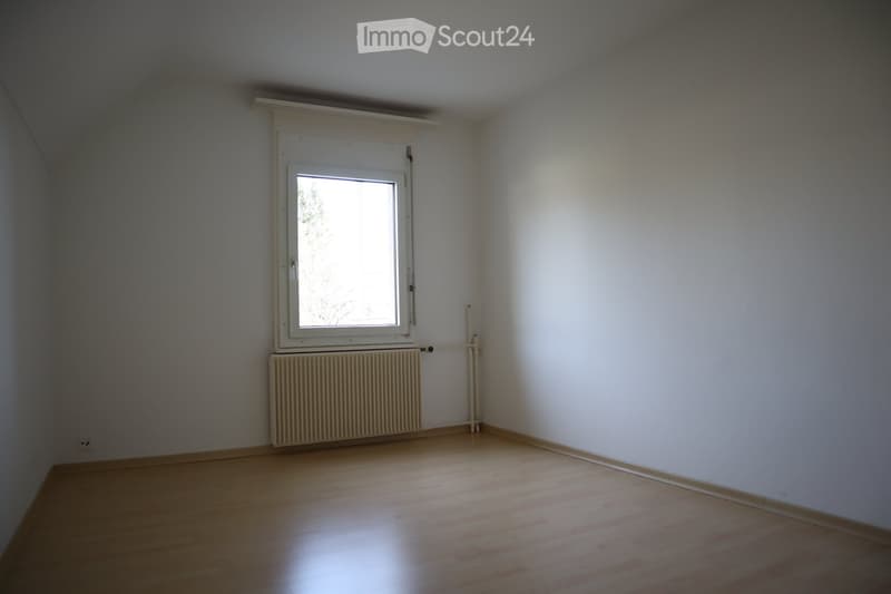 Empty room with light wooden flooring, white walls, a single window with white frame, and a radiator below the window.