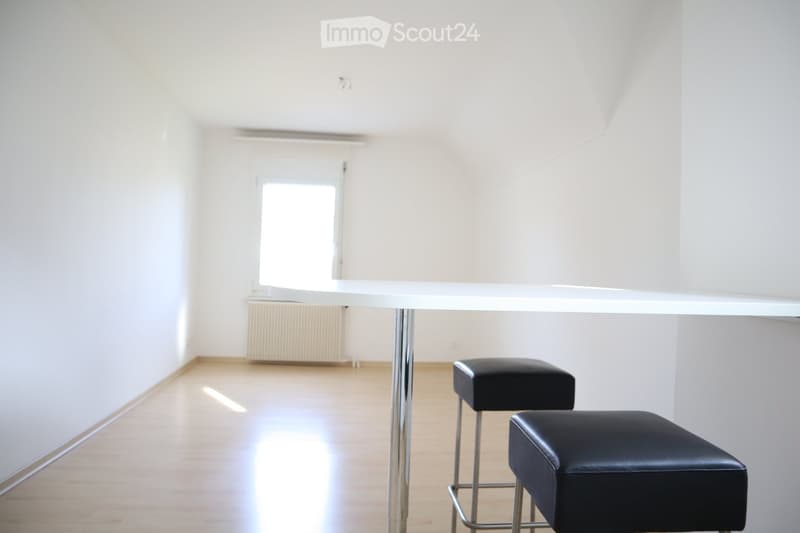 Bright, minimalist room with white walls, wooden floor, and a white table with two black stools.